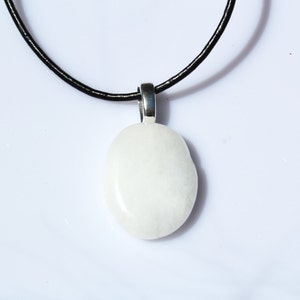 Peut inclure: Un collier avec un pendentif blanc ovale. Le pendentif est suspendu &agrave; un cordon noir. Le pendentif est fait d'un mat&eacute;riau lisse et opaque. Le fond est blanc.