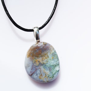 May include: A natural stone pendant necklace. The pendant is an oval shape with a silver bail and a black cord. The stone has a mix of colors, including blue, green, brown, and white.