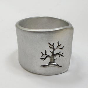 Open aluminum band ring with perforated tree perpendicular to the ring, and custom text.