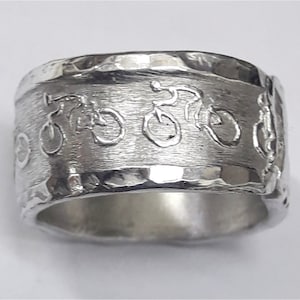 Puede incluir: Un anillo de plata con textura martillada y un diseño de cinco bicicletas alrededor de la banda.