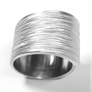 Puede incluir: Un anillo de plata con un acabado texturizado cepillado. El anillo es ancho y tiene una forma redondeada.
