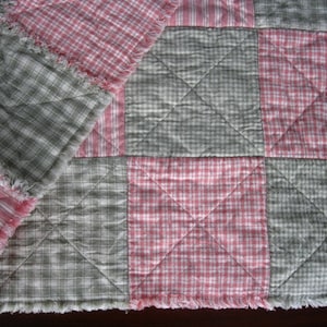 May include: A handmade quilt featuring a patchwork design with alternating squares of pink and green plaid fabric. The quilt has a fringed edge and a diamond-stitched pattern, creating a cozy, rustic aesthetic.