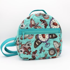 May include: A turquoise blue quilted backpack with a whimsical design featuring butterflies, clocks, and eyes. The backpack has two zipped pockets and a shoulder strap.