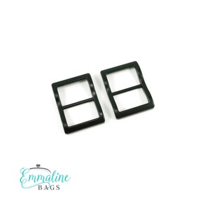 May include: Two black rectangular metal slides with a horizontal bar. These slides are for bag making and craft projects. The Emmaline Bags logo is in the bottom left corner.