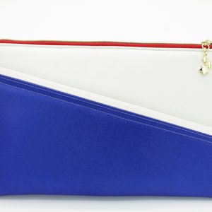 Puede incluir: Una bolsa con cremallera azul, blanca y roja con un dije de estrella dorada. La bolsa está hecha de material de imitación de cuero.