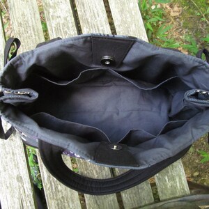 Op de afbeelding: De binnenkant van een zwarte tote bag met meerdere vakken. De tas is gemaakt van een donkere stof met een zwarte voering.