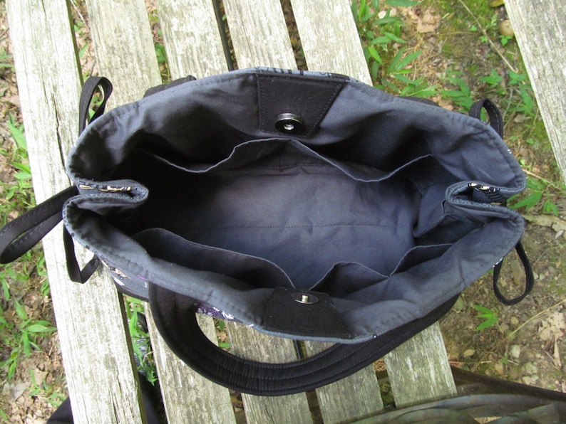 Op de afbeelding: De binnenkant van een zwarte tote bag met meerdere vakken. De tas is gemaakt van een donkere stof met een zwarte voering.