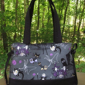 Op de afbeelding: Een zwarte tote bag met een grijze voering van stof met een herhalend patroon van personages uit de film Nightmare Before Christmas. De tas heeft zwarte hengsels en een trekkoord sluiting. De voering van stof heeft Jack Skellington, Sally, Oogie Boogie en andere personages uit de film.