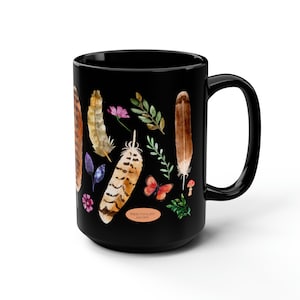 May include: Black ceramic mug with a watercolor design of feathers, flowers, and leaves. The text "RED-TAILED HAWK" is printed on the mug.