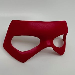 May include: A red superhero mask with a single eye hole. The mask is made of a smooth, flexible material.