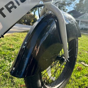 Pu&ograve; includere: Primo piano di un parafango anteriore nero su una bicicletta elettrica bianca e nera. Il parafango &egrave; fissato con bulloni argentati. Lo pneumatico &egrave; nero con la scritta "ELECTRIC BOX 3.0" sul fianco. La bici &egrave; sull'erba.
