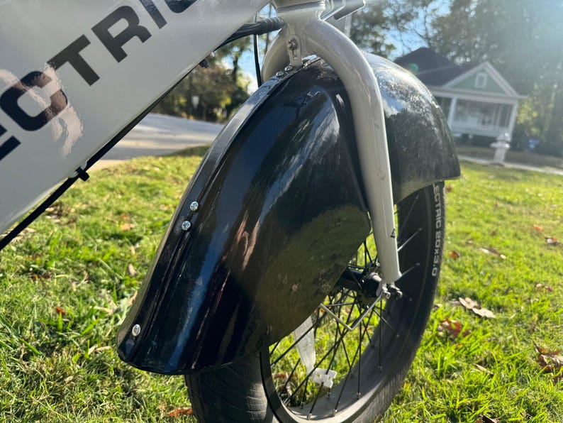 Pu&ograve; includere: Primo piano di un parafango anteriore nero su una bicicletta elettrica bianca e nera. Il parafango &egrave; fissato con bulloni argentati. Lo pneumatico &egrave; nero con la scritta "ELECTRIC BOX 3.0" sul fianco. La bici &egrave; sull'erba.