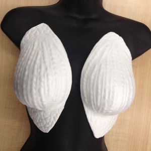 May include: A pair of white foam breast forms with a textured surface. The forms are displayed on a black mannequin.