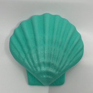 Könnte beinhalten: Ein türkisfarbenes, muschelförmiges Objekt. Das Objekt hat eine strukturierte Oberfläche mit radialen Linien, die der natürlichen Form einer Jakobsmuschel ähneln. Die Muschel hat eine einfarbige, undurchsichtige Farbe und scheint aus Schaumstoff oder einem ähnlichen Material zu bestehen.