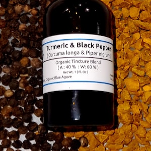 May include: A dark glass bottle with a white label displaying "Turmeric & Black Pepper" and ingredient information. The bottle is surrounded by black peppercorns and pieces of turmeric. The label also states the net weight is 1 fl oz.