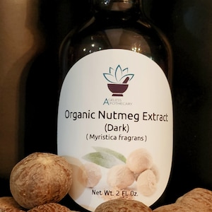 May include: A dark brown glass bottle with a black lid, labeled "Organic Nutmeg Extract (Dark) (Myristica fragrans)" and "Net Wt. 2 Fl. Oz.". The bottle is surrounded by whole nutmeg seeds.