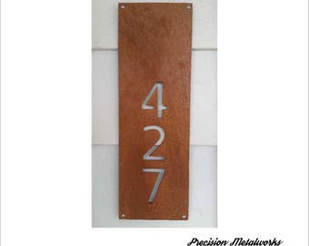 Puede incluir: Un letrero de número de casa de metal oxidado con los números 427 recortados. El letrero está montado en una pared blanca. El texto "Precision Metalworks" es visible en la parte inferior de la imagen.