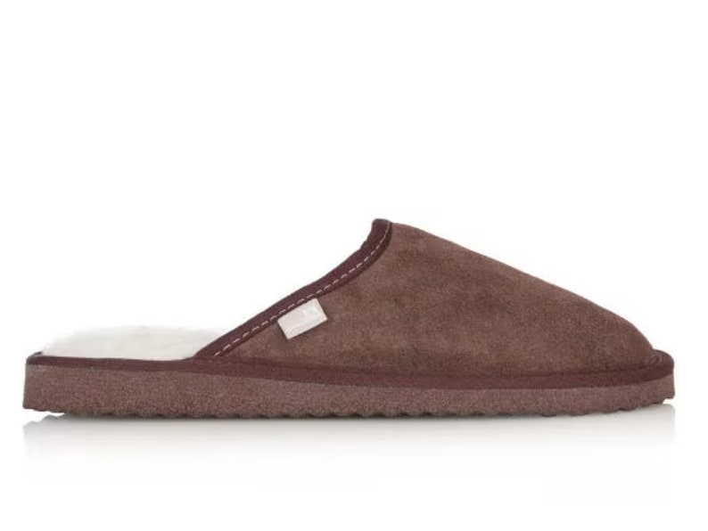 May include: Brown suede slippers with a white faux fur lining. The slippers have a closed toe and a flat sole.