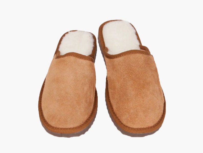 May include: A pair of brown suede slippers with a white sheepskin lining. The slippers have a closed toe and a slip-on design.
