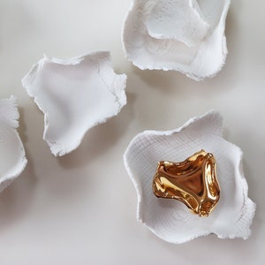 May include: Five white ceramic bowls with a single gold bowl in the center. The bowls have a textured, organic shape.