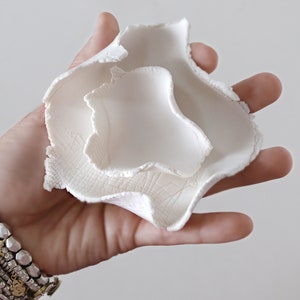 May include: White ceramic bowl with a unique, organic shape. The bowl is made of three layers, each with a slightly different texture. The bowl is perfect for holding small items, such as jewelry or keys.