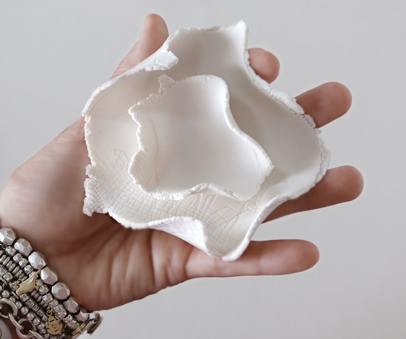 May include: White ceramic bowl with a unique, organic shape. The bowl is made of three layers, each with a slightly different texture. The bowl is perfect for holding small items, such as jewelry or keys.