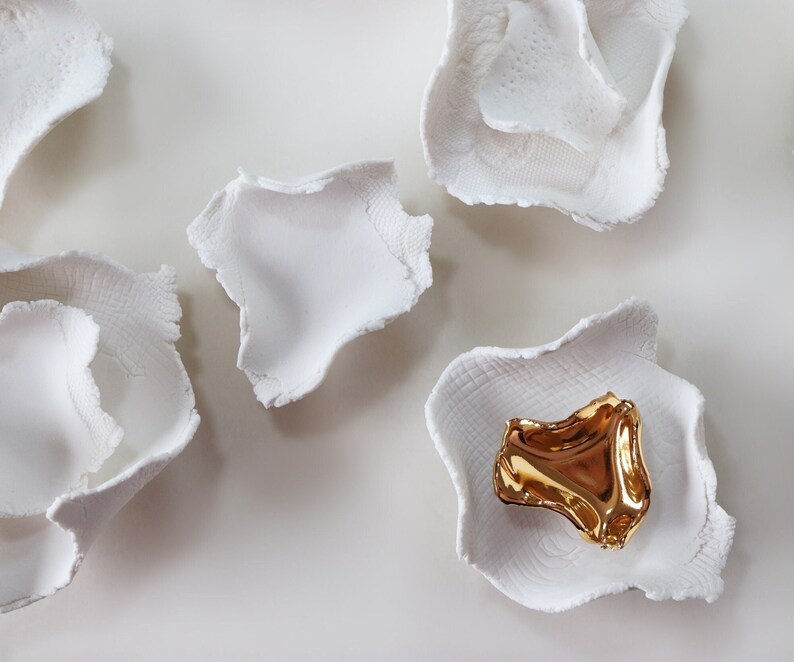 May include: Five white ceramic bowls with a single gold bowl in the center. The bowls have a textured, organic shape.