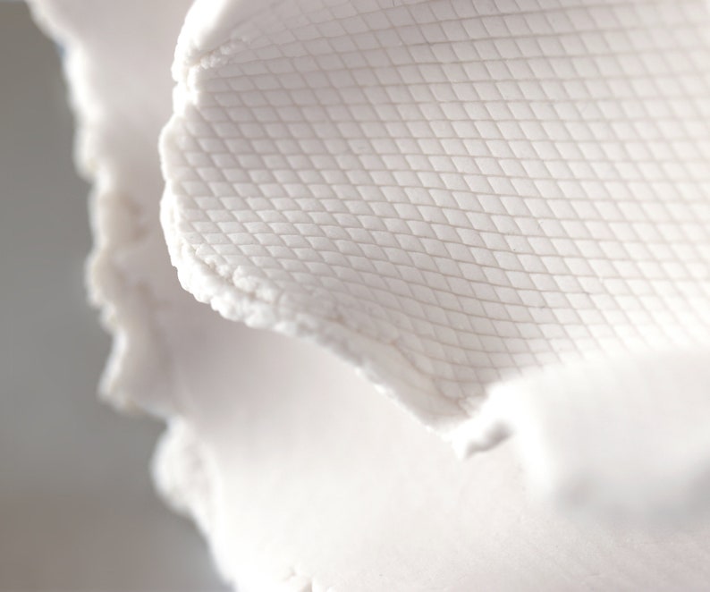 May include: Close-up of a white, textured surface with a diamond pattern. The surface is slightly curved and has a rough, uneven edge.