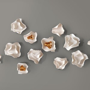 May include: A collection of white ceramic wall sculptures with gold accents. The sculptures are shaped like flowers and are arranged in a random pattern.