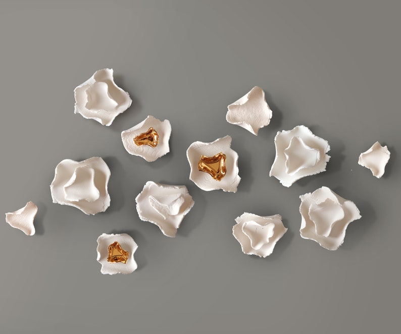 May include: A collection of white ceramic wall sculptures with gold accents. The sculptures are shaped like flowers and are arranged in a random pattern.