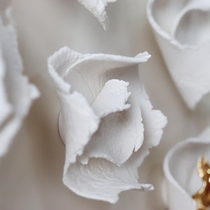 May include: Close-up of a white ceramic wall sculpture with a flower-like design. The sculpture has a textured surface and appears to be made of multiple layers of petals.