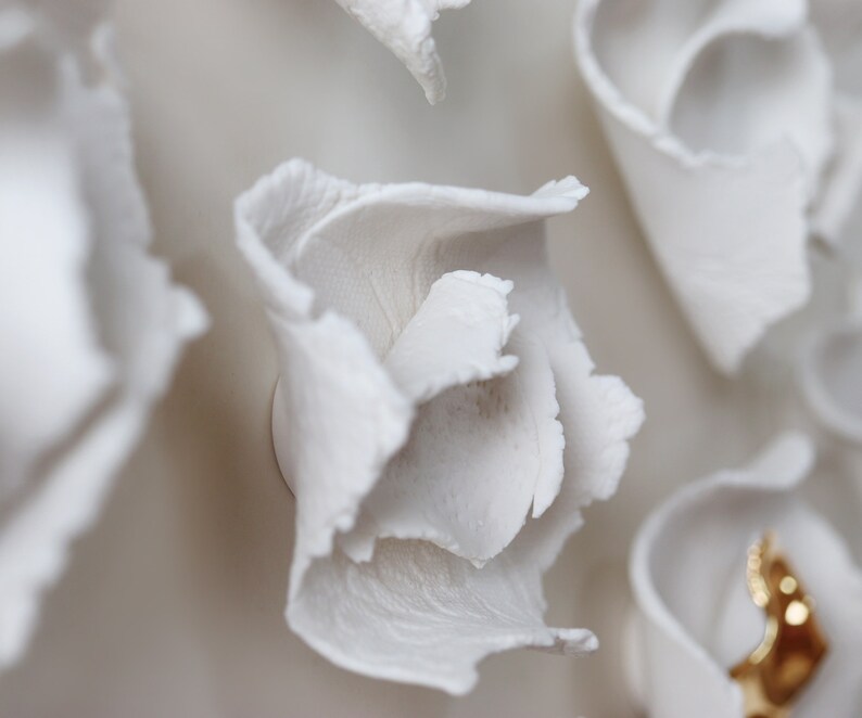 May include: Close-up of a white ceramic wall sculpture with a flower-like design. The sculpture has a textured surface and appears to be made of multiple layers of petals.