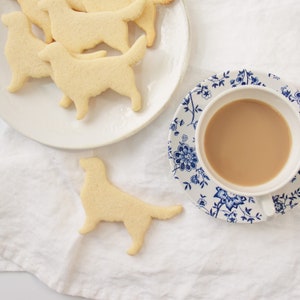 May include: A plate of dog-shaped sugar cookies with a cup of tea and a saucer with a blue and white floral pattern.