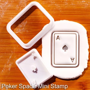 以下が含まれることがあります： 「Poker Spade Mini Stamp」の文字が入った白いプラスチック製のポーカー用スペードミニスタンプ。正方形のフレーム、カード型のスタンプ、スペードのエースが刻印されたカードが含まれています。
