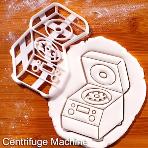 Könnte beinhalten: Ein Set aus drei Keramikbechern mit gesprenkelter, matter Oberfläche. Die Becher sind in den Farbtönen Creme, Hellgrau und Dunkelgrau gehalten. Jeder Becher hat ein schlichtes, minimalistisches Design und einen abgerundeten Henkel. Die Becher sind aufeinander gestapelt.