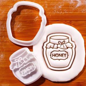 Peut inclure: Emporte-pièces en plastique blanc en forme de pot de miel. L'un est le contour du pot, un autre est la forme du pot avec le mot "HONEY", et le troisième est la forme du pot avec le mot "HONEY" à l'envers.
