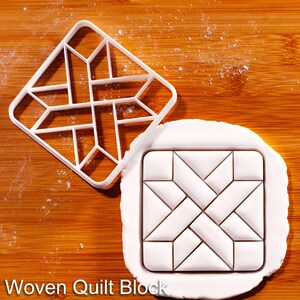 Op de afbeelding: Een witte plastic koekjesvorm met een geometrisch ontwerp, naast een wit deegblok met een geweven quiltblokpatroon. De tekst "Woven Quilt Block" staat onderaan. De achtergrond is een houten oppervlak.