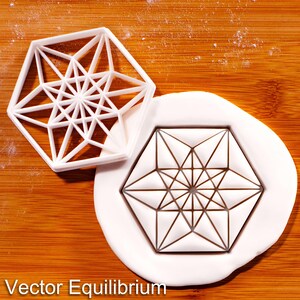 May include: A white plastic cookie cutter with a complex geometric star pattern and a matching white fondant cutout featuring the same intricate, symmetrical, multi-pointed star design. The text Vector Equilibrium is printed at the bottom.