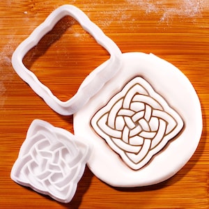 May include: White plastic cookie cutters and a fondant design with a Celtic knot pattern. The cutters include a square frame, a small square cutter, and a fondant design with a brown outline.