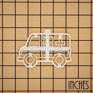 May include: White plastic cookie cutter shaped like an ambulance. The ambulance has a red cross on the side.