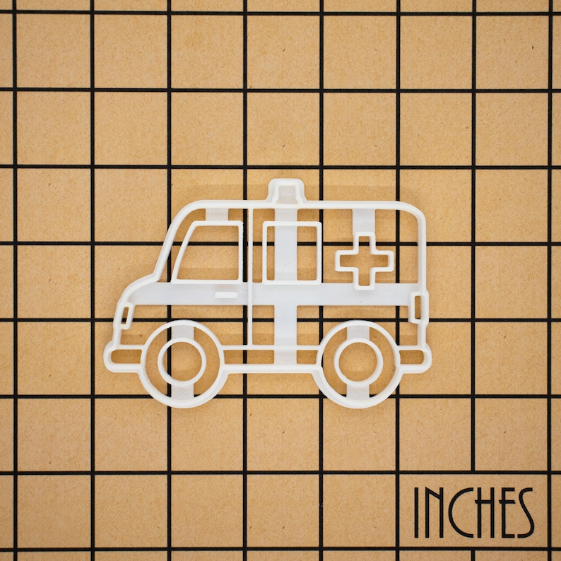 May include: White plastic cookie cutter shaped like an ambulance. The ambulance has a red cross on the side.