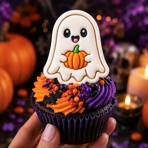 May include: A chocolate cupcake topped with orange and purple frosting, black bat-shaped sprinkles, and a large white ghost-shaped cookie holding a small orange pumpkin. The ghost has black eyes and a small open mouth, with a thin gold outline.