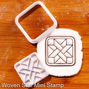 Può includere: Tagliapasta e timbro in plastica bianca su una superficie di legno. Il timbro presenta un disegno a stella intrecciata. Il testo "Woven Star Mini Stamp" è visibile nella parte inferiore dell'immagine.