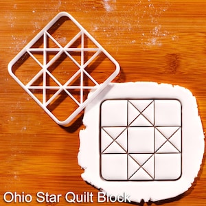 Könnte beinhalten: Ein weißer Ausstechform aus Kunststoff für Ohio Star Quilt-Blöcke mit quadratischem Rahmen und geometrischen Innenteilern, neben einem Stück weißem Fondant, das mit demselben Sternmuster geprägt ist, inklusive dem Text Ohio Star Quilt Block.
