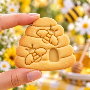 K&ouml;nnte beinhalten: Ein hell goldbrauner Keks in Form eines Bienenstocks mit gepr&auml;gten Details von zwei Bienen und einem kleinen gew&ouml;lbten Eingang. Der Keks hat eine glatte, gebackene Textur und ein abgerundetes, gestuftes Design mit klarem Abdruck.