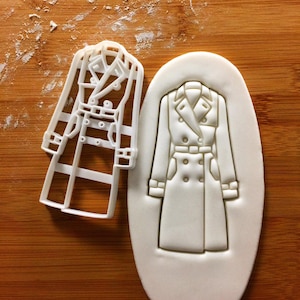 May include: A white plastic cookie cutter in the shape of a trench coat. The cookie cutter is shown next to a sample cookie that has been cut out using the cookie cutter.