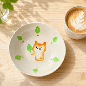 May include: A round, off-white ceramic bowl featuring a central illustration of a small orange and white fox-like creature holding a green leaf. The interior of the bowl is decorated with a repeating pattern of green leaves and small red berries.