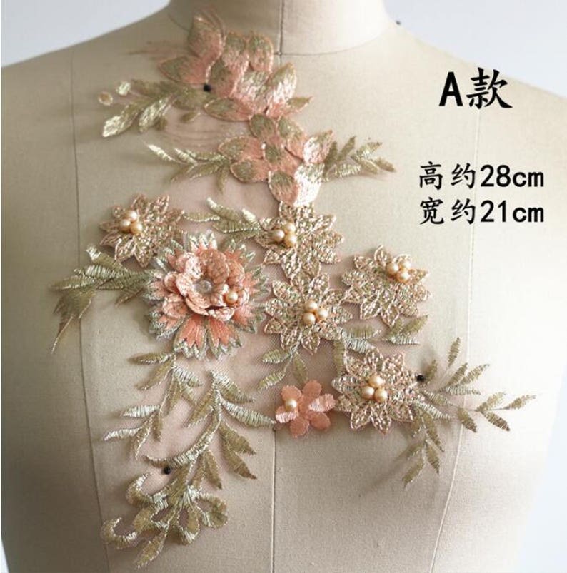 May include: A delicate floral applique with gold and peach embroidery. The applique features a variety of flowers and leaves, with pearl accents. The applique measures approximately 28 inches tall and 21 inches wide.