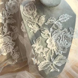 May include: White floral lace fabric with delicate embroidery and small beads. The lace features a repeating pattern of flowers and leaves.