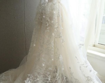 May include: A white wedding dress with a long train and delicate lace detailing. The dress has a fitted bodice and a flowing skirt. The lace is adorned with small, sparkling embellishments.